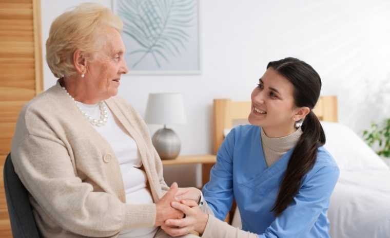 A smiling female caregiver holding hands with an elderly woman, showing compassion and emotional connection, companionship in senior home care in Pennsylvania