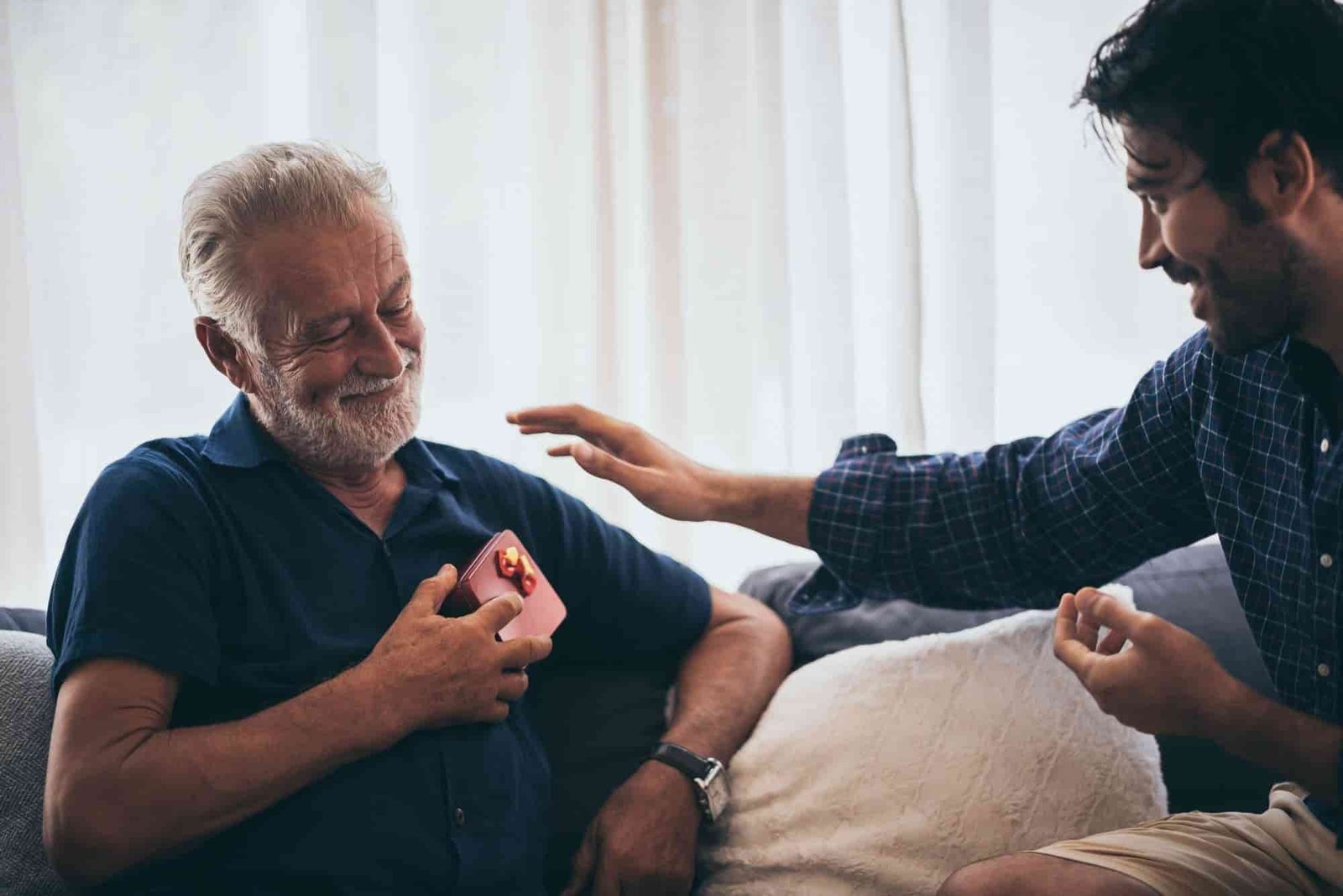 Senior man showing gratitude while receiving a small gift from a younger man, illustrating emotional connection and companionship often facilitated by home care.