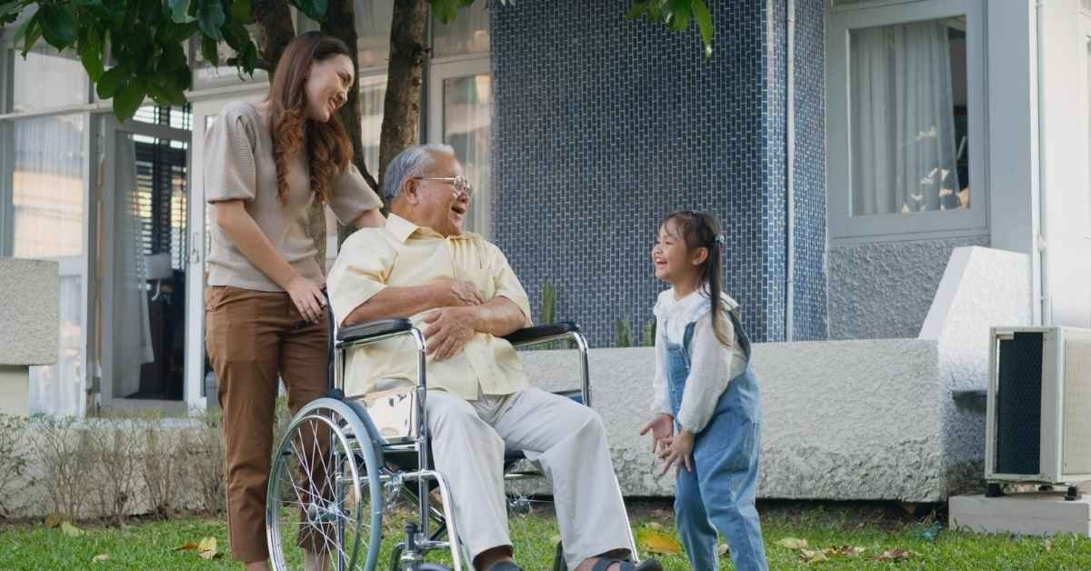 Guide to Home Care showing a senior man in a wheelchair smiling outdoors with support from a family caregiver and interaction with a young child, highlighting compassionate in-home care and family support.